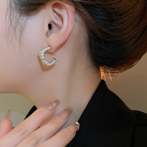 Detail view of a model wearing elegant C-shaped silver earrings with micro-set pearls
