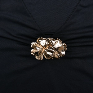 Détail d'une robe col en V élégante avec boucle fleur dorée et tissu noir plissé raffiné