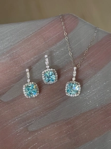Close-up of cushion-cut light blue stone pendant and earrings set with halo diamonds