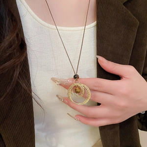 Detail of layered gold rings necklace with tiger eye stone on brown cord and white knit
