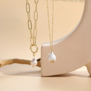 Detailed view of baroque pearl necklaces with gold paperclip links on minimalist backdrop