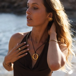 Golden sunburst earrings and jewelry set on model with a sunset water background