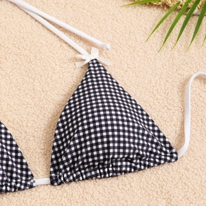 Detail of checkered bikini top with white bow and ties on beige textured background