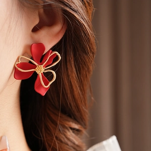 Close-up of red petal flower earrings with gold ribbon bow on a model with soft lighting