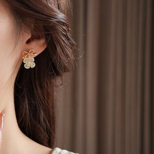 Close-up of a gold bow and shell flower pearl earring worn on a model's ear