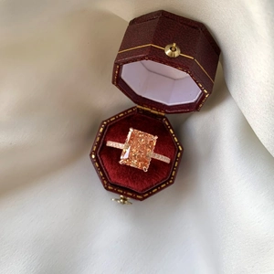 Detailed macro view of an orange-pink emerald cut gemstone ring in a vintage red gift box