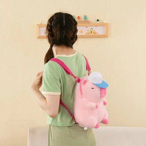 Detail of pink plush pig backpack with blue baseball cap worn by a model in soft lighting