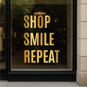 Close-up of gold foil SHOP SMILE REPEAT lettering stickers on a modern glass storefront