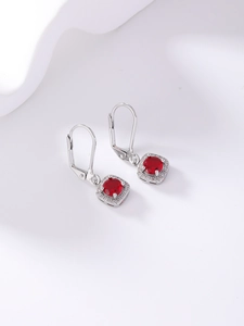 Macro detail of silver lever-back earrings with a round red gemstone and halo diamonds