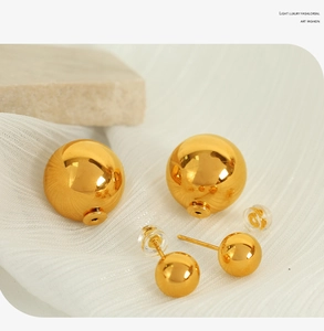 Macro detail of gold-plated double ball stud earrings on white silk and stone texture
