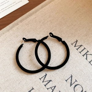 Close-up of black velvet-flocked circular hoop earrings with soft matte texture