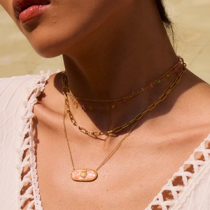 Close-up detail of 18K gold layered necklaces with pink shell pendant and colorful beads.
