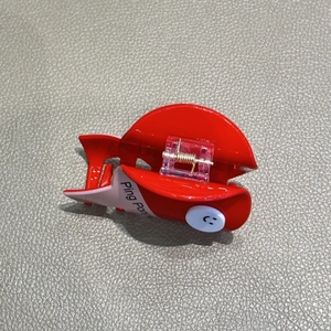 Rote Ping Pong Haarklammer mit rosa Details und Smiley auf grauem Hintergrund