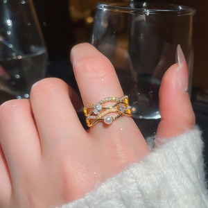 Detail of multi-layer gold wave ring with sparkling zircons and a white pearl on a hand