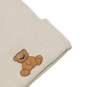 Close-up of cute brown bear embroidery on a cream knitted beanie cap texture