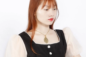 Close-up of golden leaf pendant featuring intricate hollow patterns on a long necklace