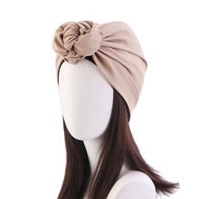 Detail of light camel knitted turban hat with rose knot decoration on a mannequin head