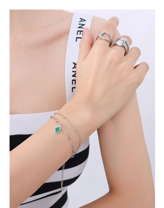 Detail of a double-layered silver bracelet with a green geometric pendant and rings on hand