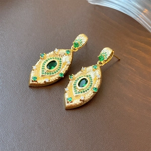 Macro shot of vintage gold earrings with emerald green and white gemstone details
