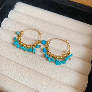 Detailed shot of golden hoop earrings with blue stones in a beige jewelry box