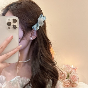 Detail of light blue satin bow hair clip with rose decoration on wavy brown hair