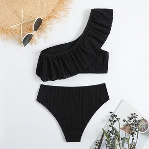 Flat lay of black one-shoulder ruffle bikini with textured fabric and summer accessories