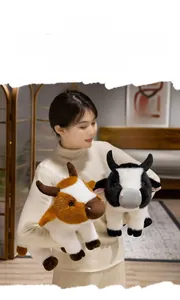 Close-up of soft brown and black stuffed cow plush dolls held by a model in a home setting