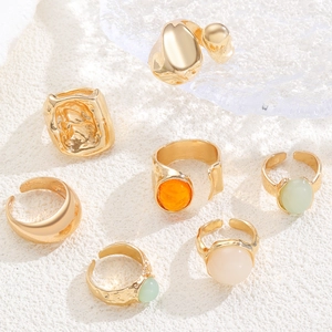 Macro detail of seven gold-plated rings with hammered textures and colorful resin stones