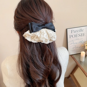 Détail d'un nœud en satin noir avec dentelle brodée blanche sur cheveux ondulés