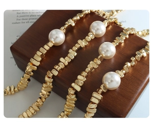 Detalle de cuentas doradas irregulares y perlas blancas sobre un joyero de madera real