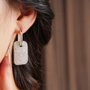 Close-up of sparkling square pavé crystal drop earrings worn on a model's ear