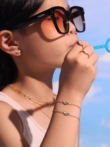 Gros plan d'un enfant portant un ensemble de bijoux nuage arc-en-ciel en acier doré et émail