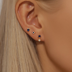 Detailed view of three gold star stud earrings with blue and white zircons on ear