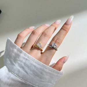 Dettaglio macro di anelli in oro e argento con zirconi a goccia indossati sulla mano