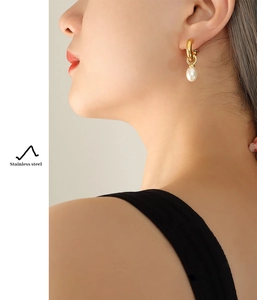 Detail of stainless steel C-shaped gold hoop earring with white drop pearl on model