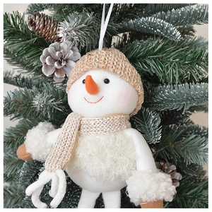 Detail of plush snowman ornament with beige knitted hat on snowy pine branch background