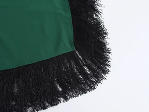 Dettaglio del tessuto verde con fitte frange nere sull'orlo del vestito lungo da donna