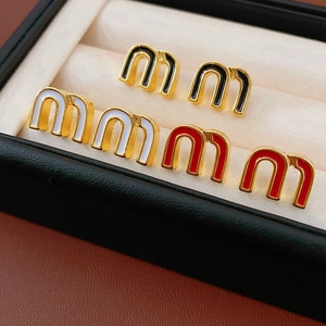 Macro detail of M-shaped enamel stud earrings in black white and red with gold trim
