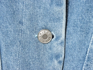 Nahaufnahme des silbernen Metallknopfs mit JEANS-Gravur auf hellblauem Jeansstoff