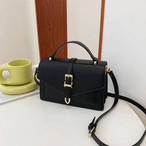 Elegant black PU leather handbag with gold buckle and adjustable strap on white table