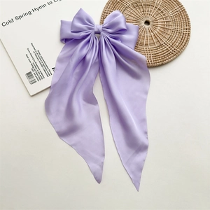 Detail of light purple satin bow hair clip with long ribbons on a textured mat