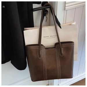 Detail of dark brown tote bag featuring contrast white stitching and long shoulder straps