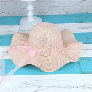 Detail of pink straw sun hat featuring wavy brim with delicate lace flower and pearl