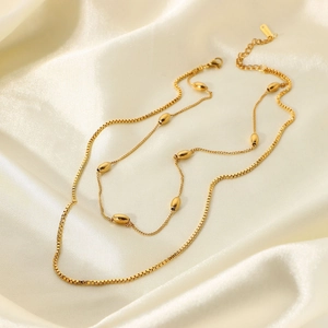 Detail view of double-layered 18K gold plated necklace with oval beads on white silk
