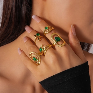 Detail of four gold rings set with green stones worn by a model in warm light