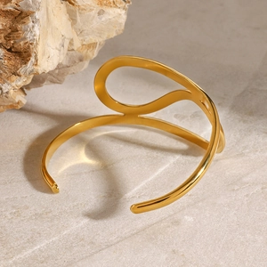 Nahaufnahme des goldenen geometrischen Armreifs mit 18K-Glanz auf Marmorhintergrund