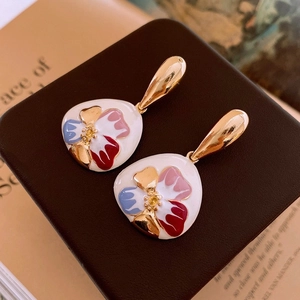 Macro shot of French style floral earrings with colorful enamel glaze on a vintage book