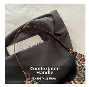 Detail der Leopardenmuster-Tasche mit braunem Ledergriff und goldener Hardware auf grauem Blazer