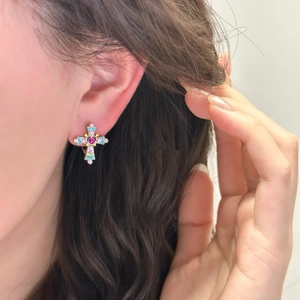 Close-up of a silver cross earring with colorful gemstones worn on a female ear