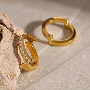 Minimalist gold C-shaped earrings with white zircon accents on natural stone base